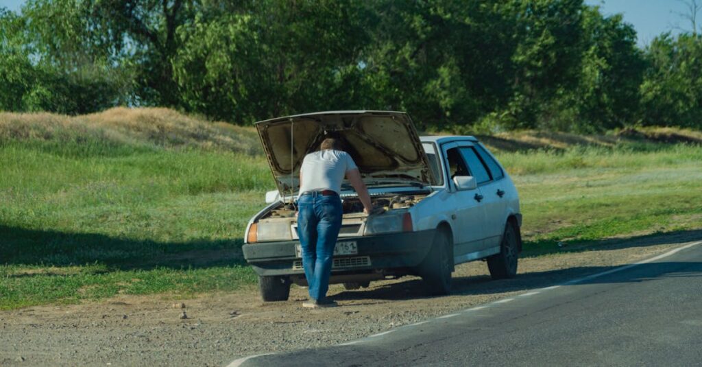 A man stands by his car on the roadside, inspecting a breakdown issue.